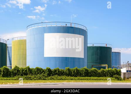 Large coloured storage tanks for oil and fuel in an oil terminal with a white blank copy space under a blue sky. Stock Photo