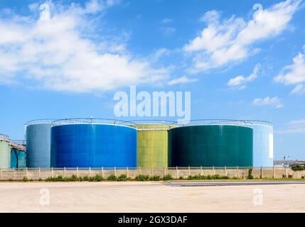 Large coloured storage tanks for oil and fuel in a tank farm under a blue sky with white clouds. Stock Photo