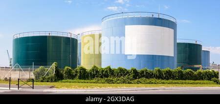 Panoramic view of large coloured storage tanks for oil and fuel in an oil terminal with a white blank copy space under a blue sky. Stock Photo