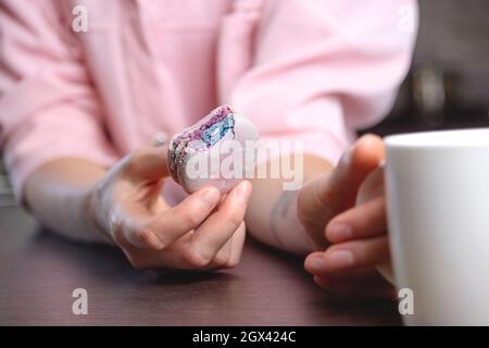 Bitten macaron in woman's hand next to cup of tea. Close up texture. Stock Photo