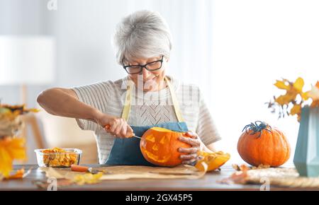 Happy Halloween! Senior woman is carving pumpkin. Family preparing for holiday. Stock Photo