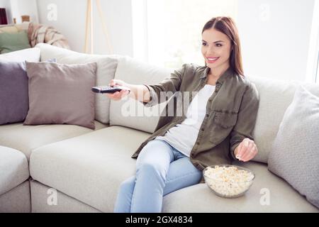 Photo of sweet charming young lady wear green shirt smiling eating pop corn changing channels indoors room home Stock Photo