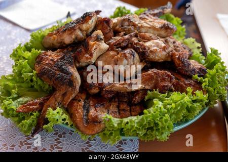 Charcoal-fried chicken wings lie on green salad leaves on a porcelain platter, ready to eat. Stock Photo