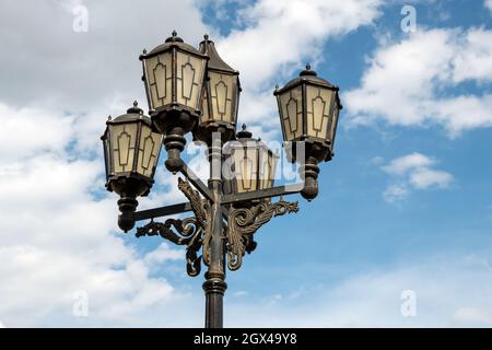 Old-style urban street electric lamp against the background of the summer sky. Stock Photo