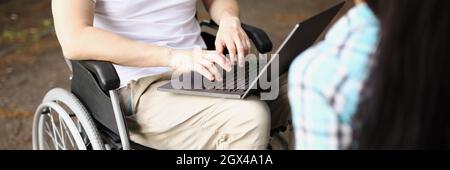 Man in wheelchair works on laptop on street next to woman sits and holds tablet Stock Photo