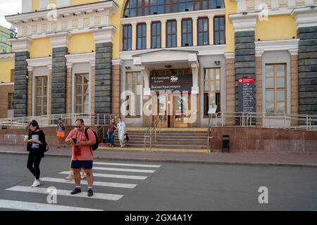 People walk along the pedestrian crossing from the central entrance of the city's main railway station with an electronic scoreboard in Russian. Stock Photo