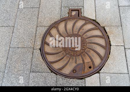 Cast iron manhole cover is located on the pavement of gray concrete tiles. Stock Photo