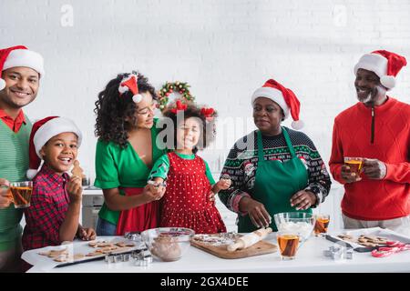 happy girl holding cookie cutter while preparing christmas cookies with african american family Stock Photo