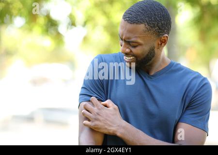 Black man scratching itchy arm walking in a park Stock Photo