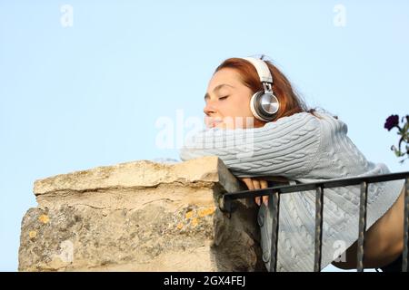Satisfied woman wearing wireless headphones listening to music resting in a balcony Stock Photo