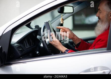 Bearded senior man holding phone and texting while sitting in car a parking lot Stock Photo