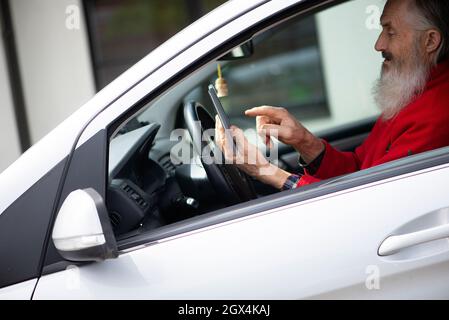 Bearded senior man holding phone and texting while sitting in car a parking lot Stock Photo