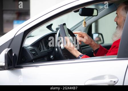 Bearded senior man holding phone and texting while sitting in car a parking lot Stock Photo