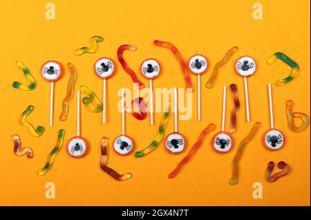 Halloween candy with black spiders,cobweb and tasty jelly worms on orange color background,top view Stock Photo