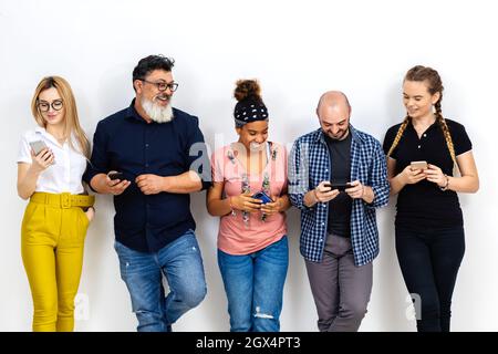 Multiracial friends laughing while using mobile phones against wall Stock Photo