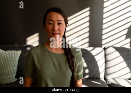 Portrait of serious asian woman sitting on sofa at home Stock Photo