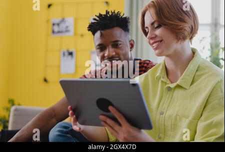 Young biracial couple using tablet, having fun indoors at home, checking social networks together. Stock Photo