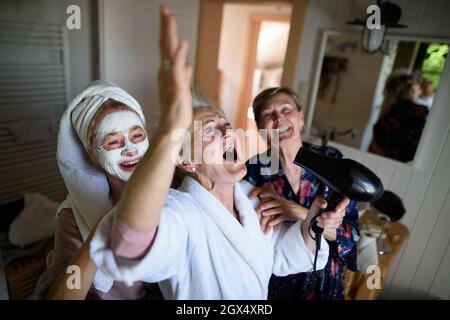 Happy senior women friends in bathrobes having fun indoors at home, selfcare concept. Stock Photo