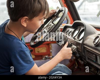 An 11-year-old boy enthusiastically plays the driver behind the wheel of an old abandoned car. Stock Photo