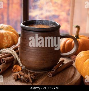 Closeup of a steaming mug of hot chocolate and mini pumpkins by a window with colorful autumn background Stock Photo