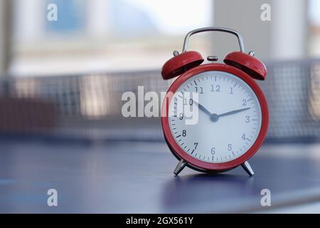 Red alarm clock standing on tennis table closeup Stock Photo