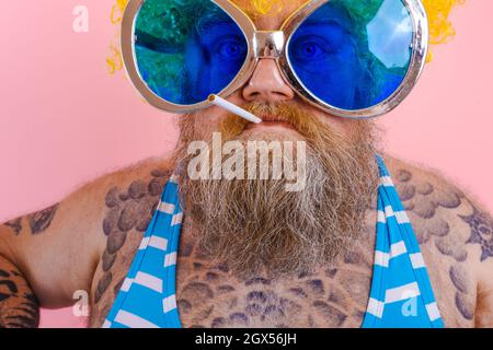 Fat angry man with beard and wig smokes cigarettes Stock Photo