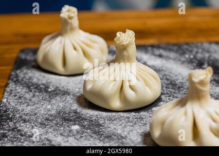Georgian dumplings Khinkali with meat, on a wooden board with flour, black background. Process of making cooking khinkali Stock Photo