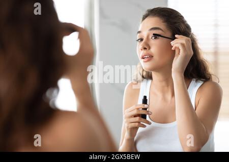 Attractive Lady Applying Mascara On Eyelashes In Modern Bathroom Stock Photo