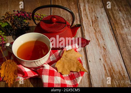 on a wooden table a red teapot, a white cup with tea, yellow and red autumn leaves, black berries Stock Photo