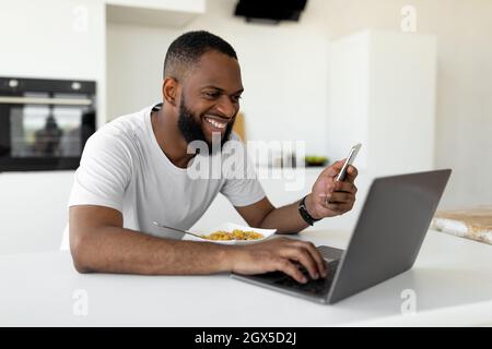Black man using pc and smartphone having breakfast at home Stock Photo