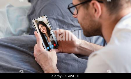 Young man using smartphone for web chat with his asian girlfriend Stock Photo