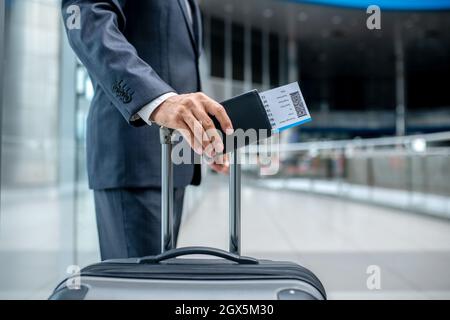 Mans hand with ticket touching handle of suitcase Stock Photo