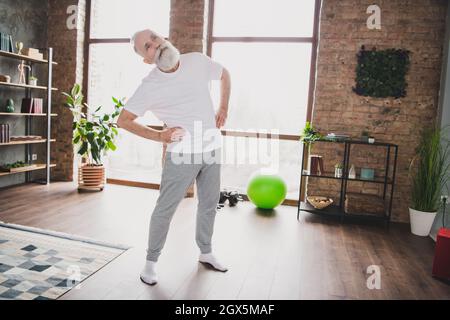 Full size photo of handsome sportive mature man athlete stretching spine body exercising training at home house Stock Photo