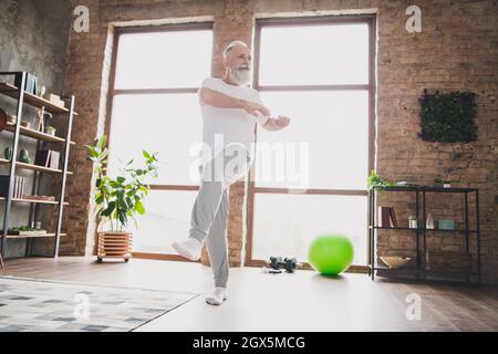 Full size photo of focused concentrated mature man warming up stretching legs doing cardio exercising at home house Stock Photo