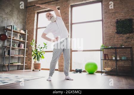 Full size photo of focused concentrated mature man grandfather exercising stretching spine hands at home house Stock Photo