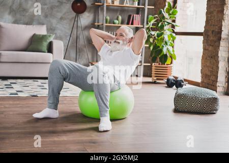 Full size photo of happy positive handsome grandfather exercising abdomen using fitball training at home house Stock Photo