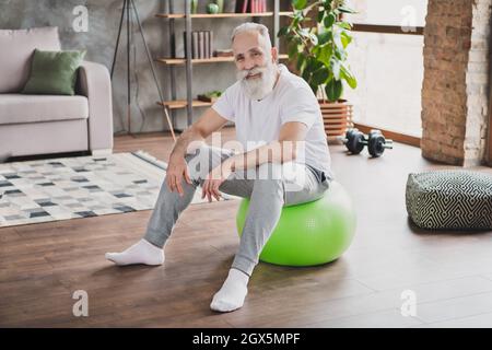 Full size photo of handsome cheerful good mood smiling handsome mature man relaxing at fitball at home house Stock Photo