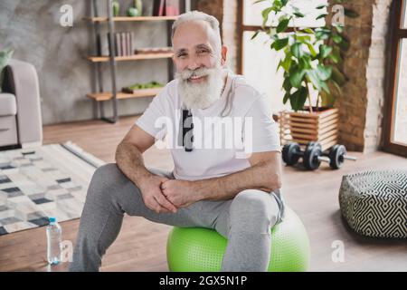 Photo of positive cheerful old man wear sportive clothes sit green fit ball pensioner indoors inside house home gym Stock Photo