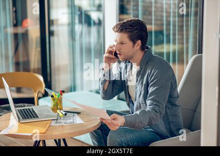 Profile of man talking on smartphone sitting at laptop Stock Photo