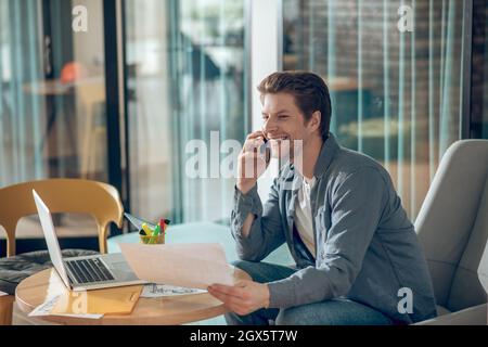 Joyful man at workplace talking on smartphone Stock Photo