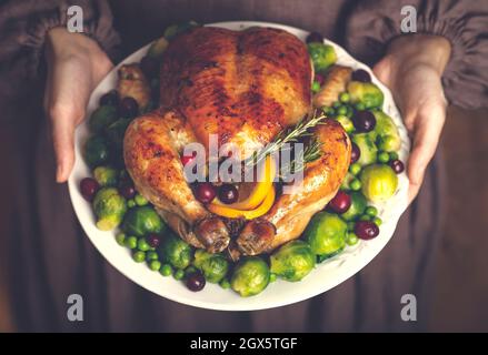 Thanksgiving turkey or chicken for a festive dinner. A plate of fried chicken in the hands of a woman in a classic American dress. Thanksgiving and autumn seasonal food concept. High quality photo Stock Photo