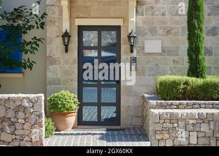 Modern house facade with stone finished wall, glass door and bushes in europe Stock Photo