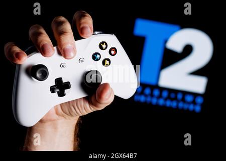 A white gamepad clutched in the hand on the black background  with the logo of Take-Two. Stock Photo