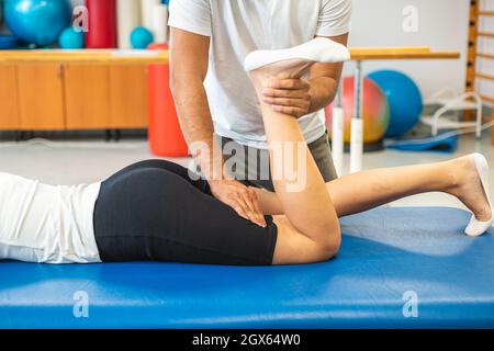 Female patient and male physiotherapist during rehabilitation treatment. Bending and straightening the leg at the knee. Stock Photo