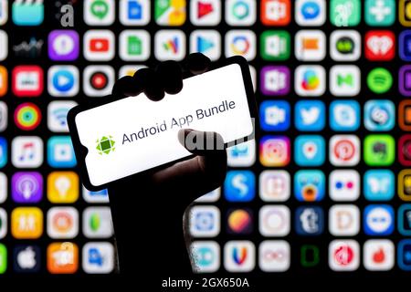 A smartphone with the AAB (Android App Bundle) logo in a clenched hand. Many apps icons on the background. Stock Photo