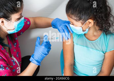 children's nurse injecting arm of little brown girl. girl watching nurse, doctor's hands with rubber gloves injecting covid-19 vaccine. flu vaccine. m Stock Photo