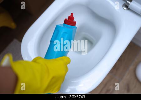 Cleaner in yellow rubber gloves pouring detergent under rim of toilet closeup Stock Photo