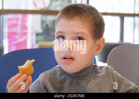 A boy of 4 years old eats nuggets with sauce in a fast food cafe. Stock Photo