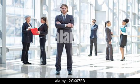 Hansome young businessman in formal suit standing in front of colleagues in business building Stock Photo