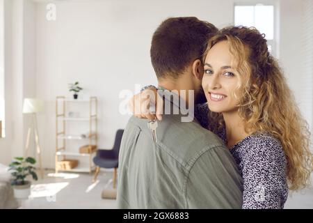 Young woman holding keys hugging husband in their new home after buying real estate. Stock Photo